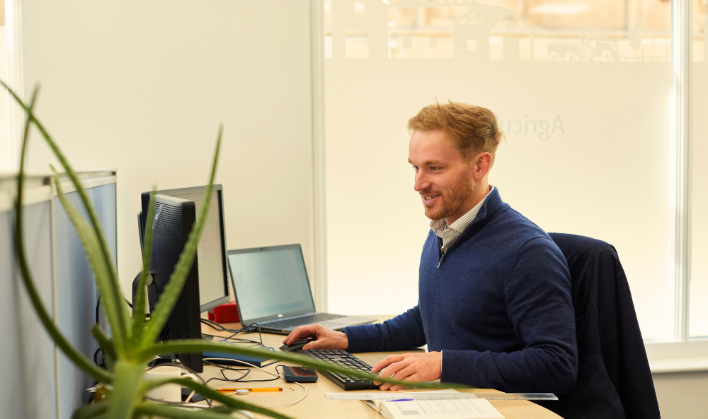 Commercial Agency Image of team member at their desk in Norwich with green plant in the foreground