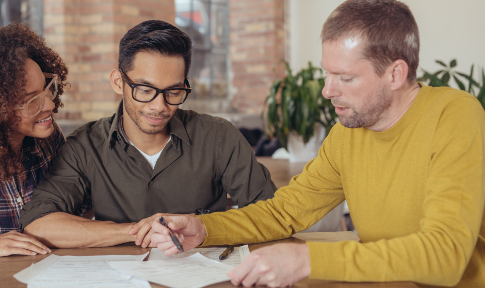 Mortgages Page - Yellow Bricks Mortgages Partnership, man in yellow jumper advising a couple of people with papers in front of them